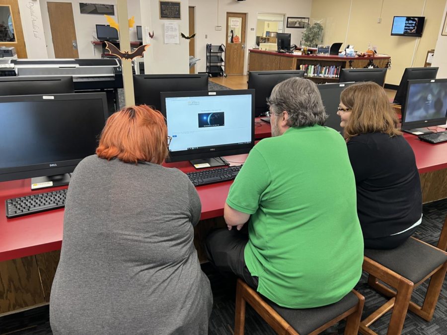 Stanley Library staff, Rachel Walton (left), Danny Adams (middle), and Sierra Alley (right), gather around the computer to start up a round of Misinformation in the Space Age.