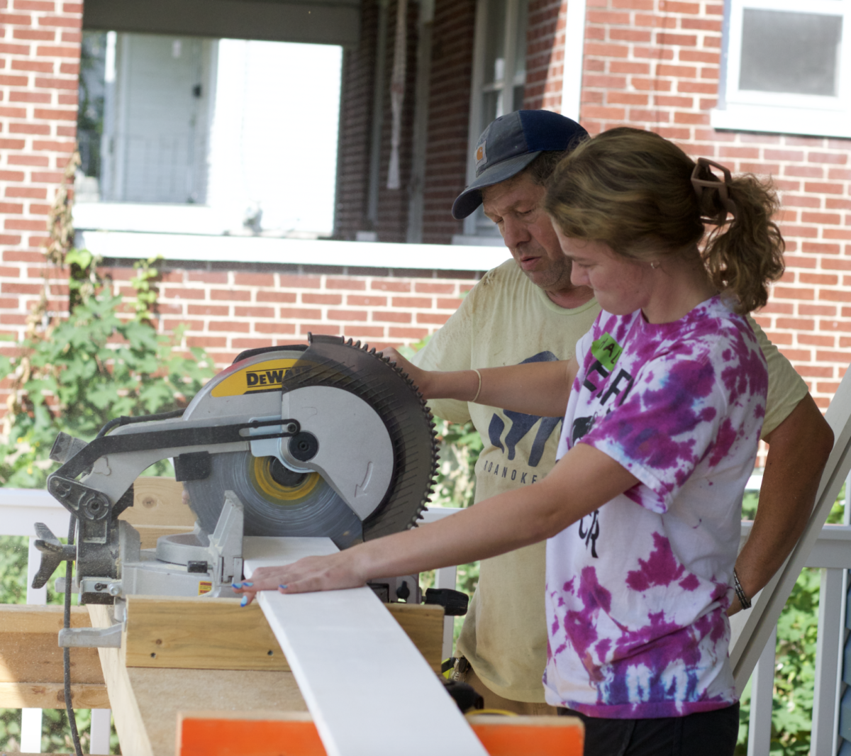 Haley Woodward, junior, right, uses a chop saw while Tony Clarke, construction site supervisor for Habitat for Humanity in the Roanoke Valley, oversees the work. 