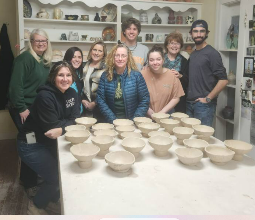 Local residents gather around their work with a smile as they complete a successful session of bowl-making for the Empty Bowls event.