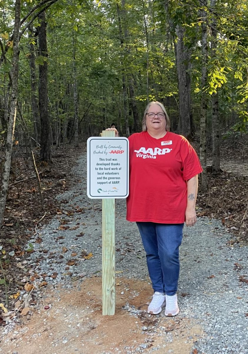 Virginia AARP Representative Angela Snyder poses with the entrance sign at the Ferrum Park ADA Accessibility Trail after speaking to the community at the opening event. 