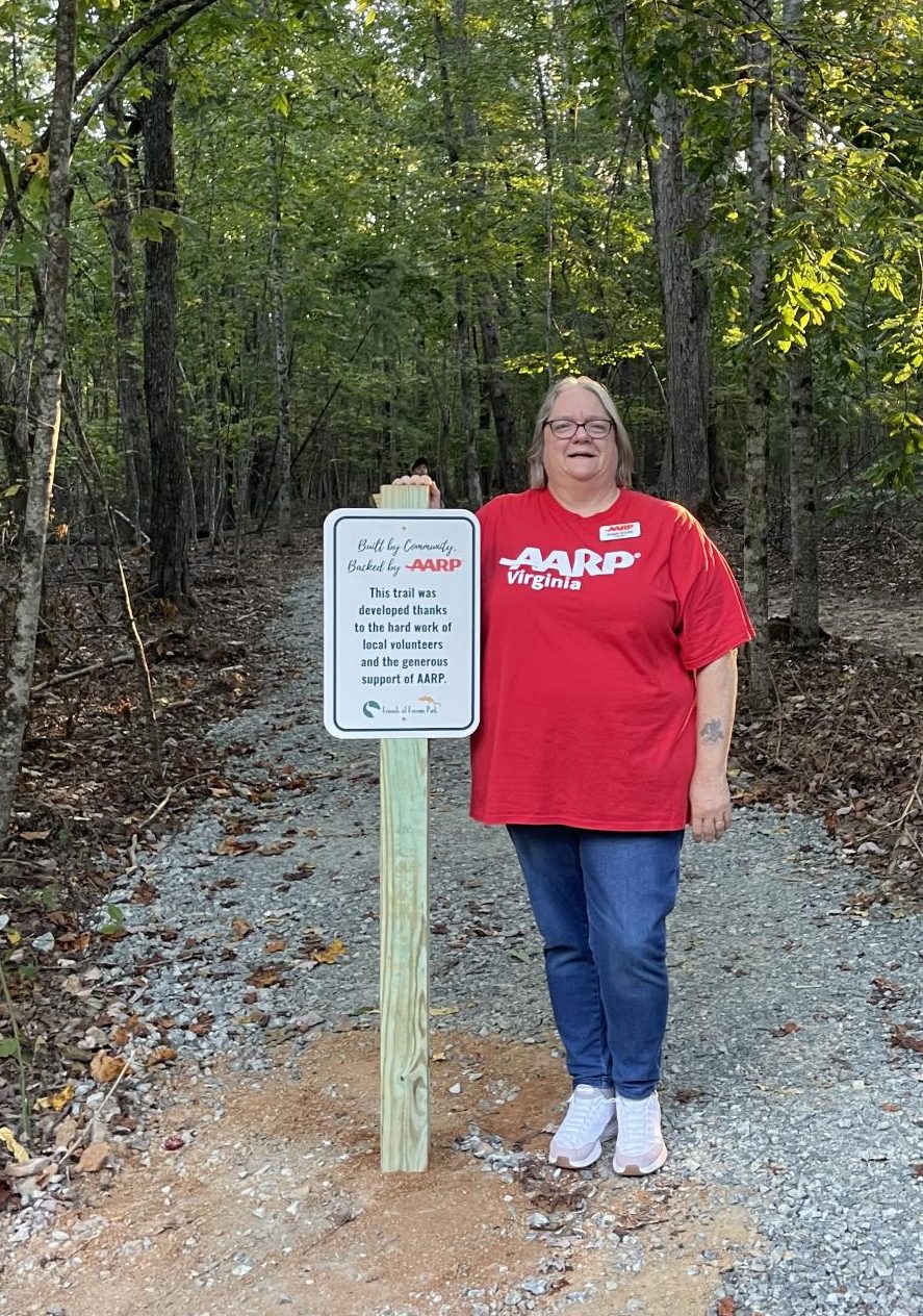 Virginia AARP Representative Angela Snyder poses with the entrance sign at the Ferrum Park ADA Accessibility Trail after speaking to the community at the opening event. 