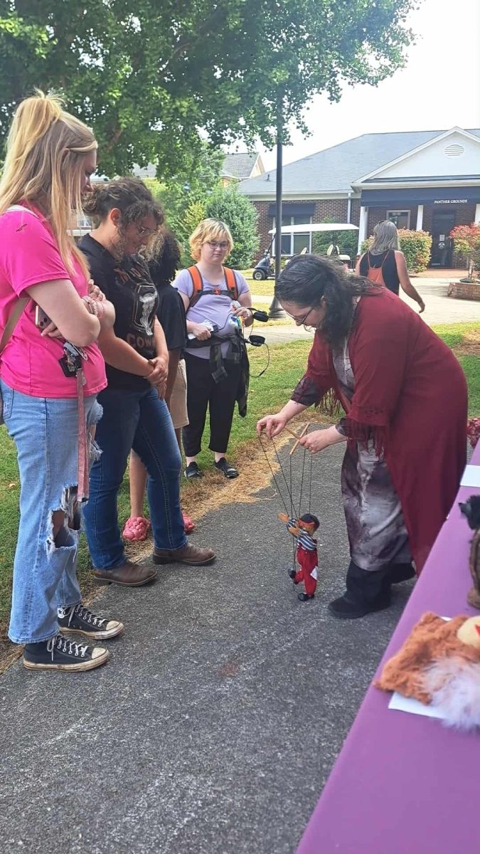 Theatre Arts Professor Rebecca Crocker presents a marionette to the students in the courtyard.